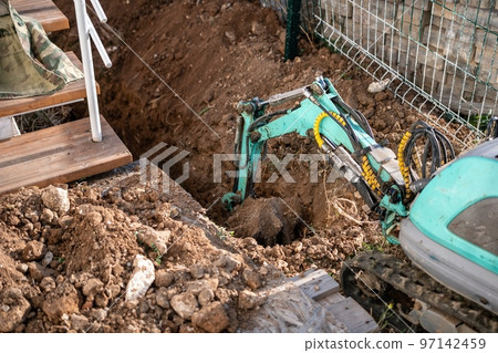 Mini excavator digs a trench to lay pipes. Close up of an excavator digging a deep trench. An excavator digs a trench in the countryside to lay a water pipe. Slow motion 97142459