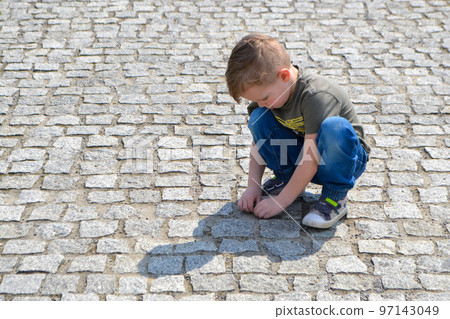 Boy sitting on the cracked earth and shows tongue. Boy five years old sits on a city pavement. High quality photo 97143049