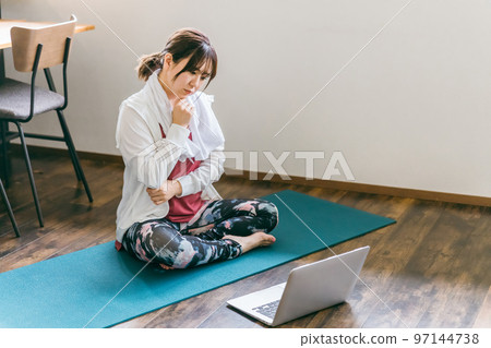 Asian woman doing yoga while using a laptop in the living room at home (worried/worried) 97144738