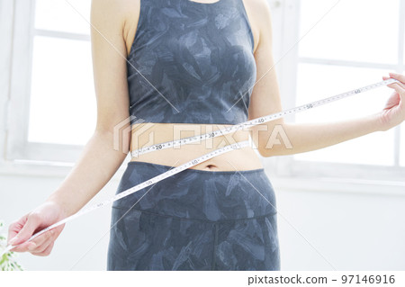 A woman measuring her waist with a tape measure, no face 97146916