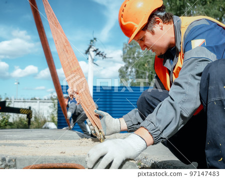 Slinger lays concrete slab on construction site on summer day. Worker in protective vest and Slinger lays concrete slab on construction site on summer day. Worker in protective vest and 97147483