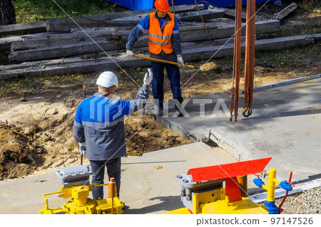Two workers in construction helmets and overalls laying concrete slab on construction site on summer 97147526