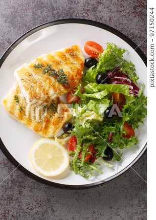 Grilled cod fillet served with fresh vegetable salad close-up in a plate. Vertical top view Grilled cod fillet served with fresh vegetable salad close-up in a plate. Vertical top view 97150244