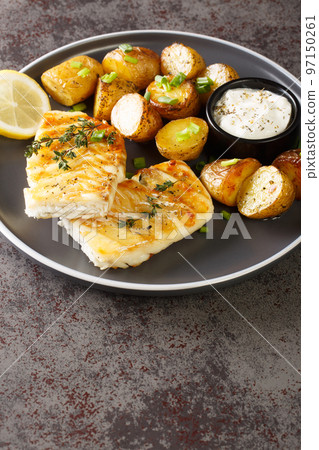 grilled cod fish with baked jacket potatoes, cream sauce and lemon close-up in a plate. Vertical grilled cod fish with baked jacket potatoes, cream sauce and lemon close-up in a plate. Vertical 97150261