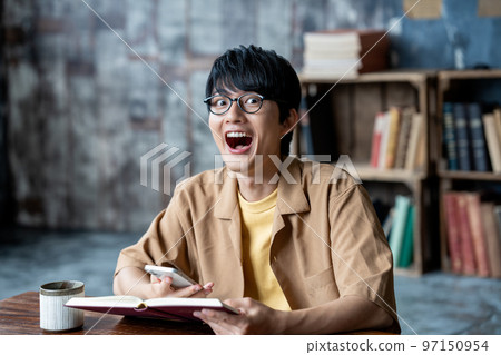 Young man with glasses using smartphone while reading Young man with glasses using smartphone while reading 97150954