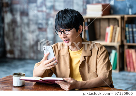 Young man with glasses using smartphone while reading 97150960