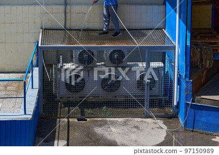 A worker washes cleans the air conditioning system in the backyard of a factory 97150989