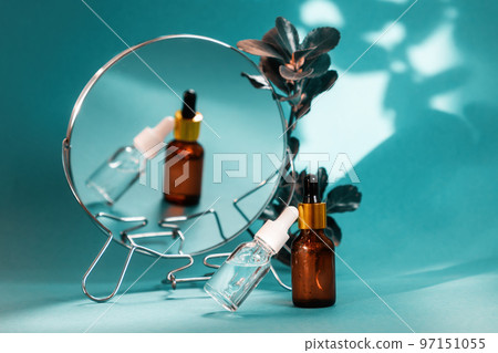 Close up of two glass bottle of cosmetic on turquoise background with mirror and leaves. Concept of herbal organic beauty products Close up of two glass bottle of cosmetic on turquoise background with mirror and leaves. Concept of herbal organic beauty products 97151055