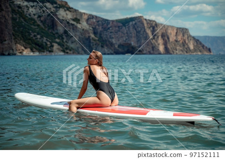 Woman sap sea. Sports girl on a surfboard in the sea on a sunny summer day. In a black bathing suit, he sits on a sapa in the sea. Rest on the sea. 97152111
