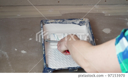 The worker's arm dips the roller into white paint to paint the wall The worker's arm dips the roller into white paint to paint the wall 97153970