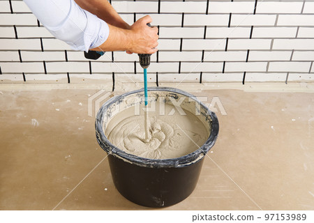 the master mixes the plaster in a bucket. Flat house renovation, master mixed the mortar in a plastic bucket with mixer the master mixes the plaster in a bucket. Flat house renovation, master mixed the mortar in a plastic bucket with mixer 97153989