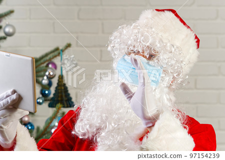 Man in Santa claus costume and Flu Mask with a Tablet Computer. congratulations from santa claus via tablet. Man in Santa claus costume and Flu Mask with a Tablet Computer. congratulations from santa claus via tablet. 97154239