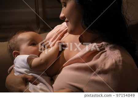 Woman breastfeeding her little baby on sofa in evening 97154849