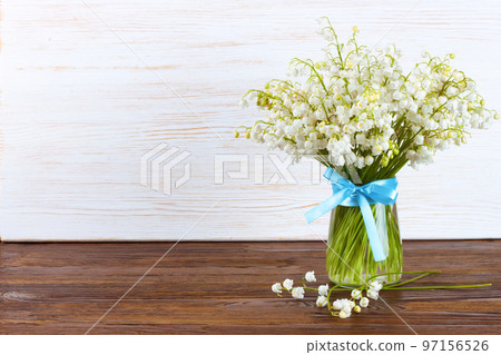 bouquet of lilies of the valley in a vase with blue ribbon on a brown white wooden background bouquet of lilies of the valley in a vase with blue ribbon on a brown white wooden background 97156526