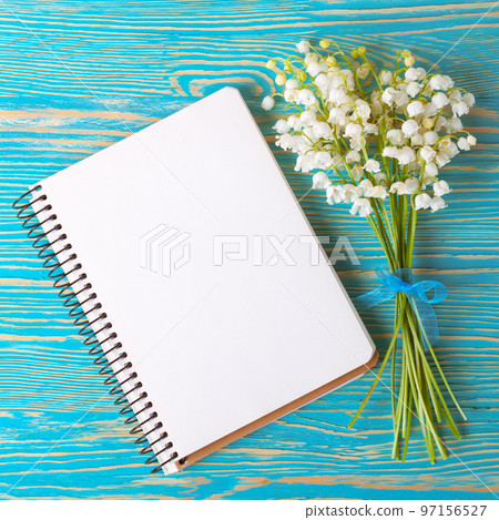 Bouquet of flowers lily of the valley and empty paper notebook on blue rustic table. 97156527