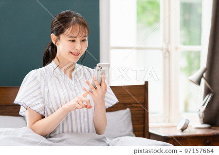 Young woman using smartphone in bedroom 97157664