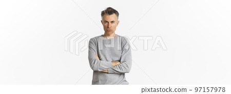 Image of angry middle-aged man feeling offended, cross arms on chest and squinting at camera, standing over white background 97157978