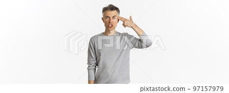 Image of annoyed and fed up middle-aged man showing finger gun sign near head, shooting himself with pissed-off face, standing tired over white background 97157979