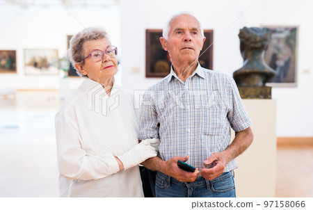mature European couple examines paintings in an exhibition in hall of art museum 97158066