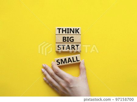 Think big start small symbol. Concept words Think big start small on wooden blocks. Beautiful yellow background. Businessman hand. Business and Think big start small concept. Copy space 97158700
