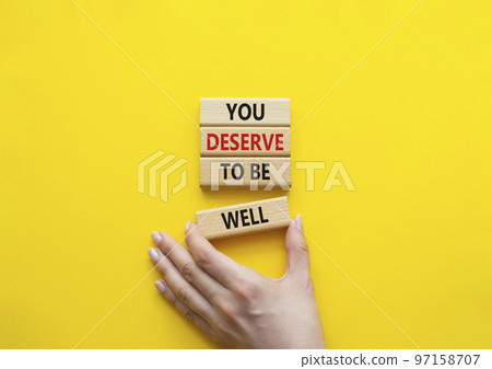 You deserve to be well symbol. Wooden blocks with words You deserve to be well. Beautiful yellow background. Businessman hand. You deserve to be well concept. Copy space. 97158707