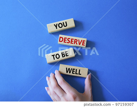 You deserve to be well symbol. Wooden blocks with words You deserve to be well. Beautiful blue background. Businessman hand. You deserve to be well concept. Copy space. 97159307