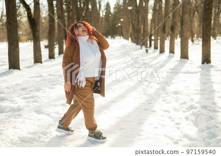 A fat woman listens to music with headphones and dances in the park in winter.  97159540