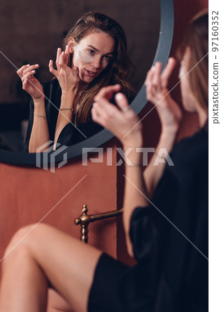 Young woman with patches under her eyes in front of the bathroom mirror Young woman with patches under her eyes in front of the bathroom mirror 97160352