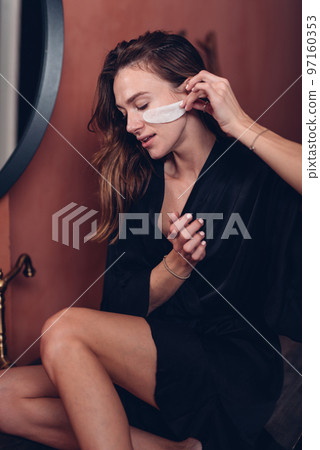 Young woman applies patch under her eyes to nourish her skin Young woman applies patch under her eyes to nourish her skin 97160353