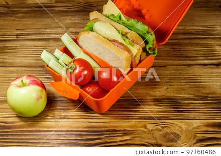 Apple and lunch box with sandwiches and fresh vegetables on a wooden table Apple and lunch box with sandwiches and fresh vegetables on a wooden table 97160486