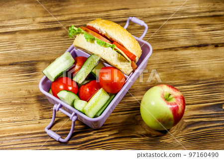 Apple and lunch box with burgers and fresh vegetables on a wooden table Apple and lunch box with burgers and fresh vegetables on a wooden table 97160490