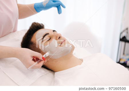 Cosmetologist applying clay mask on man's face in spa salon. Beautician make beuty for handsome man in beauty studio Cosmetologist applying clay mask on man's face in spa salon. Beautician make beuty for handsome man in beauty studio 97160500