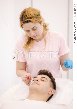 Cosmetologist applying clay mask on man's face in spa salon. Beautician make beuty for handsome man in beauty studio 97160514