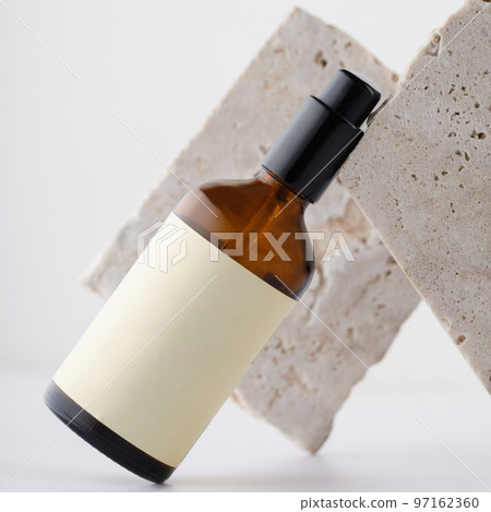 Brown glass bottle with a pump for cosmetics. Beige empty label. Against the background of travertine stones. 97162360
