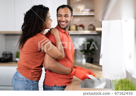 Cleaning at free time at home. Happy pretty young black woman hugging man in rubber gloves 97162450