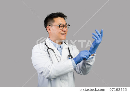 Smiling mature chinese man therapist in white coat, glasses puts on protective gloves on hands Smiling mature chinese man therapist in white coat, glasses puts on protective gloves on hands 97162533
