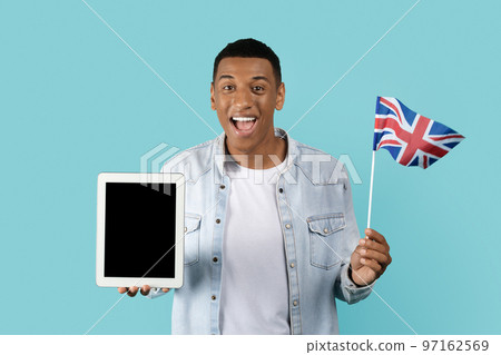 Cheerful young african american man student with open mouth show England flag, tablet with empty screen Cheerful young african american man student with open mouth show England flag, tablet with empty screen 97162569