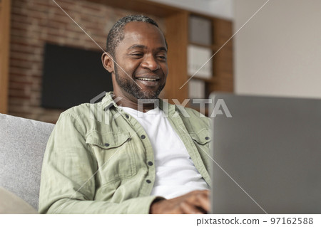 Cheerful mature black man typing on computer, has video call, enjoy communication due social distance Cheerful mature black man typing on computer, has video call, enjoy communication due social distance 97162588