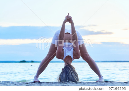 young woman practicing hatha yoga on the shore of a lake. 97164293