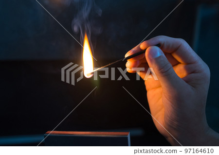 A Match ignited by rubbing the match head against a match box. Hand with burning match A Match ignited by rubbing the match head against a match box. Hand with burning match 97164610