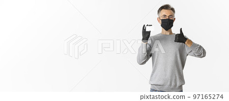 Concept of covid-19, social distancing and lifestyle. Satisfied middle-aged man in medical mask, gloves and glasses, recommending bank, showing credit card and thumbs-up Concept of covid-19, social distancing and lifestyle. Satisfied middle-aged man in medical mask, gloves and glasses, recommending bank, showing credit card and thumbs-up 97165274
