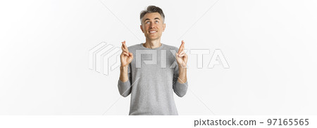 Image of excited and hopeful middle-aged man making a wish, begging God, cross fingers for good luck and looking up, standing over white background 97165565