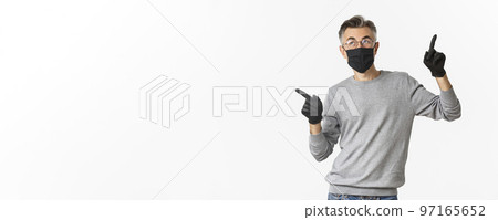 Concept of coronavirus, lifestyle and quarantine. Image of middle-aged man with grey hair, wearing black medical mask, gloves and glasses, pointing fingers sideways, showing copy space Concept of coronavirus, lifestyle and quarantine. Image of middle-aged man with grey hair, wearing black medical mask, gloves and glasses, pointing fingers sideways, showing copy space 97165652
