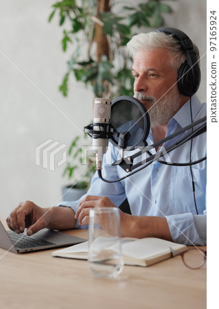 older man with gray hair irecording podcast in recording studio with microphone and headphones older man with gray hair irecording podcast in recording studio with microphone and headphones 97165924