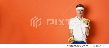Image of handsome middle-aged male athlete, workout with dumbbells and smiling, training against orange background 97167108