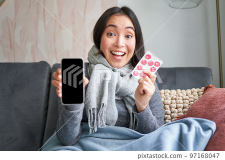 Online doctors and healthcare. Smiling korean woman shows mobile phone screen and medication, catching cold, staying at home and recommending smartphone GP Online doctors and healthcare. Smiling korean woman shows mobile phone screen and medication, catching cold, staying at home and recommending smartphone GP 97168047