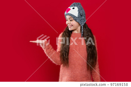 teen girl in winter fashion hat isolated on red, presenting product. teen girl wear sweater 97169158