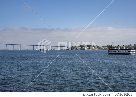 Ship sailing on San Diego bay and distant view of Coronado bridge over seascape with cloudy sky in the background during sunny day Ship sailing on San Diego bay and distant view of Coronado bridge over seascape with cloudy sky in the background during sunny day 97169265