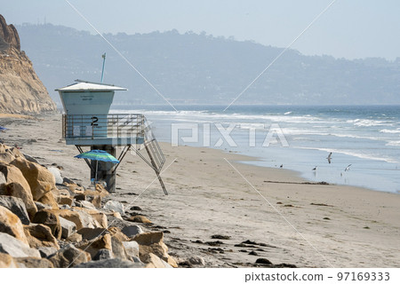 View of lifeguard hut on sandy beach and scenic view of waves splashing in sea with mountain and clear sky in the background at San Diego during sunny day View of lifeguard hut on sandy beach and scenic view of waves splashing in sea with mountain and clear sky in the background at San Diego during sunny day 97169333