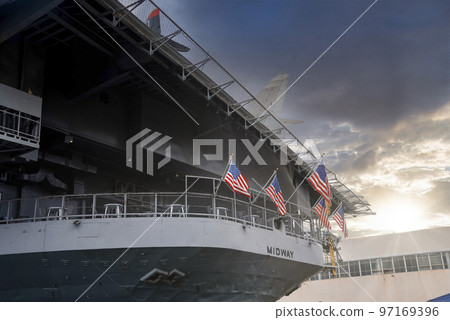 San Diego, USA. September 20, 2022. American flags waving on large USS Midway aircraft carrier below cloudy sky during sunset San Diego, USA. September 20, 2022. American flags waving on large USS Midway aircraft carrier below cloudy sky during sunset 97169396